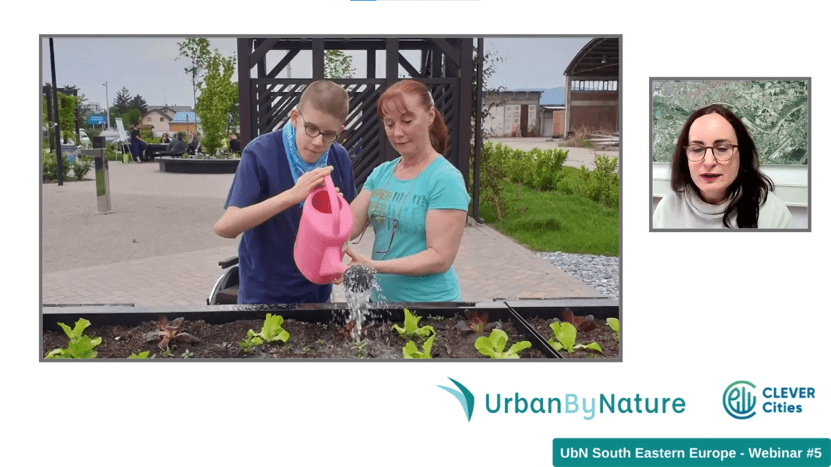 Two young people water plants in a raised bed.
